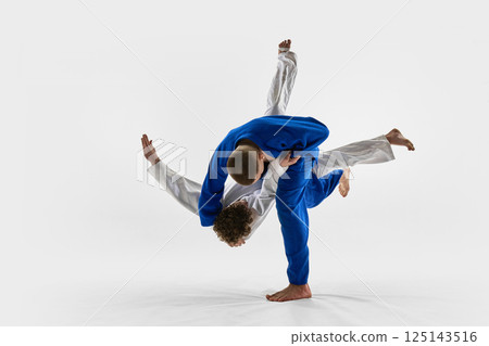 Blue gi fighter thrown over shoulder in fast motion by white gi athlete against white studio background. Concept of judo, combat sport Blue gi fighter thrown over shoulder in fast motion by white gi athlete against white studio background. Concept of judo, combat sport 125143516