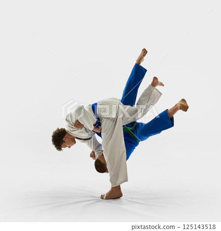 Two young athletes in mid-air judo throw, one executing perfect hip movement while opponent flies with legs up, symbolizing combat competition. Two young athletes in mid-air judo throw, one executing perfect hip movement while opponent flies with legs up, symbolizing combat competition. 125143518