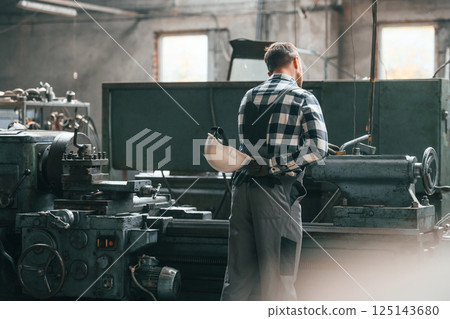 Rear view. Operating machine. Factory male worker in uniform is indoors 125143680
