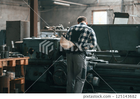 Rear view. Operating machine. Factory male worker in uniform is indoors 125143682