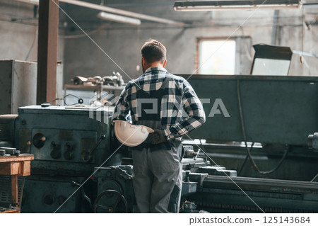 Rear view. Operating machine. Factory male worker in uniform is indoors 125143684