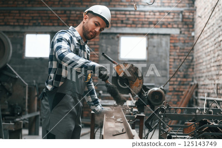 Working by operating machine. Factory worker in uniform is indoors Working by operating machine. Factory worker in uniform is indoors 125143749