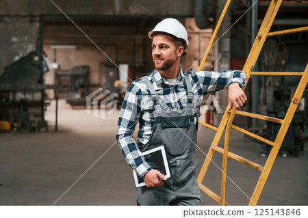 Leaning on the ladder. Factory male worker in uniform is indoors Leaning on the ladder. Factory male worker in uniform is indoors 125143846