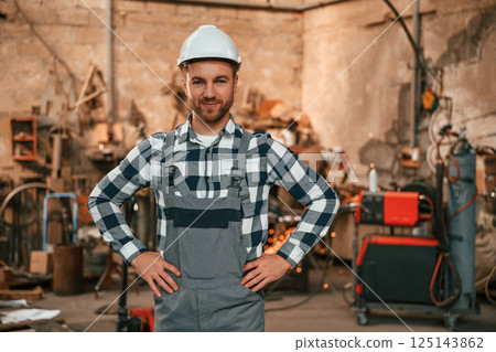 Standing, hands is on the waist. Factory male worker in uniform is indoors Standing, hands is on the waist. Factory male worker in uniform is indoors 125143862