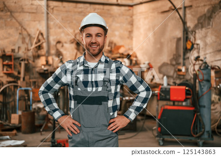 Standing, hands is on the waist. Factory male worker in uniform is indoors Standing, hands is on the waist. Factory male worker in uniform is indoors 125143863