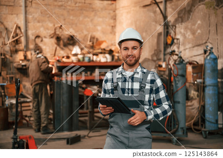 Many objects behind. Factory male worker in uniform is indoors Many objects behind. Factory male worker in uniform is indoors 125143864