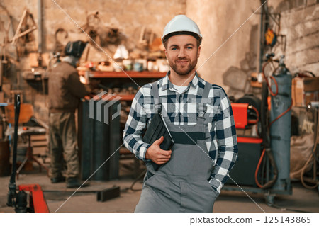 Many objects behind. Factory male worker in uniform is indoors Many objects behind. Factory male worker in uniform is indoors 125143865