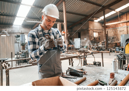 Using professional tools. Factory male worker in uniform is indoors Using professional tools. Factory male worker in uniform is indoors 125143872