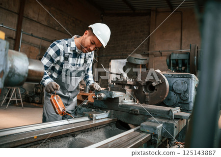 Side view. Using machine. Factory male worker in uniform is indoors 125143887