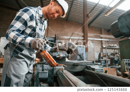 Side view. Using machine. Factory male worker in uniform is indoors 125143888