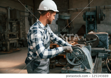 Side view. Using machine. Factory male worker in uniform is indoors 125143889