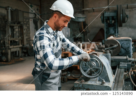 Side view. Using machine. Factory male worker in uniform is indoors 125143890
