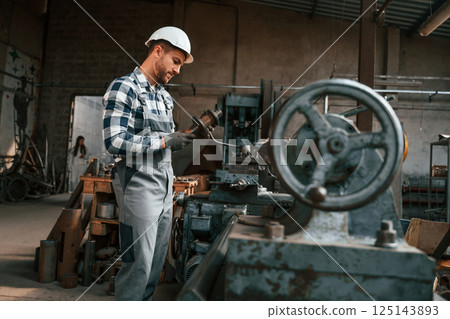Metal processing. Factory male worker in uniform is indoors Metal processing. Factory male worker in uniform is indoors 125143893