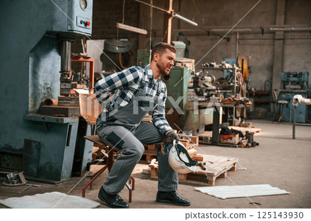 Felling bad. Back is hurting. Factory male worker in uniform is indoors Felling bad. Back is hurting. Factory male worker in uniform is indoors 125143930