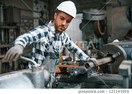 Factory male worker in uniform is indoors. With industry machine Factory male worker in uniform is indoors. With industry machine 125143959