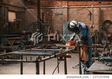 Factory worker in protective mask is welding the iron Factory worker in protective mask is welding the iron 125143998