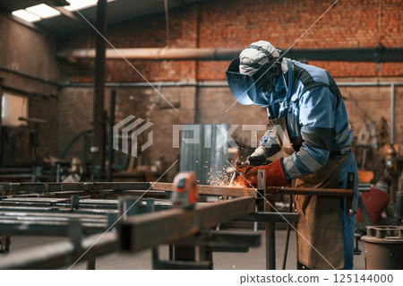 Factory worker in protective mask is welding the iron 125144000