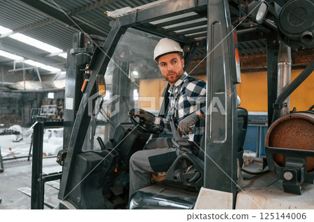 Inside of the forklift. Factory male worker in uniform is indoors Inside of the forklift. Factory male worker in uniform is indoors 125144006