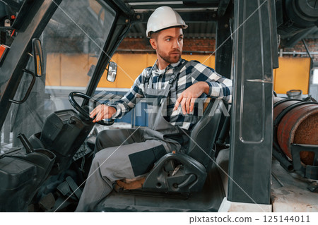 Driving the forklift. Factory male worker in uniform is indoors 125144011