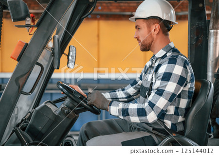 Driving the forklift. Factory male worker in uniform is indoors 125144012