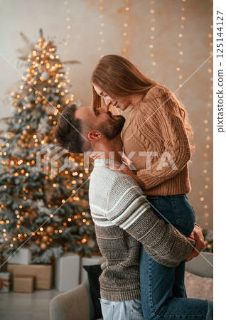 Man raised and holds the woman in his hands. Lovely young couple are celebrating New Year at home 125144127