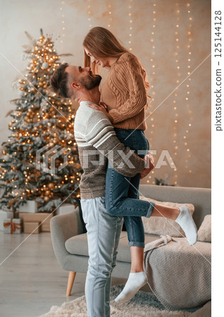 Man raised and holds the woman in his hands. Lovely young couple are celebrating New Year at home 125144128
