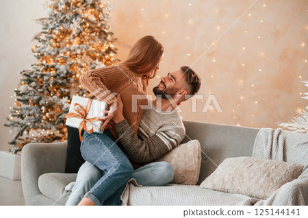 Woman is with gift box for the man. Lovely young couple are celebrating New Year at home 125144141