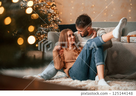 Sitting on the floor together. Lovely young couple are celebrating New Year at home Sitting on the floor together. Lovely young couple are celebrating New Year at home 125144148