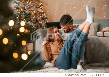 Sitting on the floor together. Lovely young couple are celebrating New Year at home 125144149