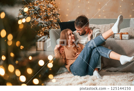 Sitting on the floor together. Lovely young couple are celebrating New Year at home Sitting on the floor together. Lovely young couple are celebrating New Year at home 125144150
