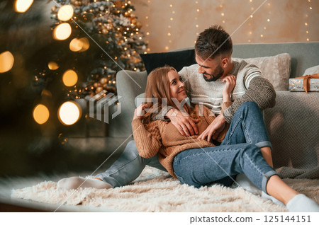 Sitting on the floor together. Lovely young couple are celebrating New Year at home 125144151
