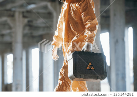 The case with biohazard sign on it. Man dressed in chemical protection suit in the ruins of the post apocalyptic building 125144291
