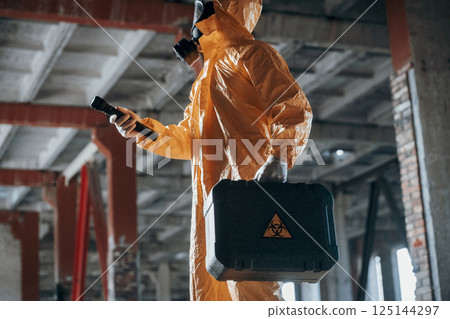 View from the side. Man dressed in chemical protection suit in the ruins of the post apocalyptic building 125144297