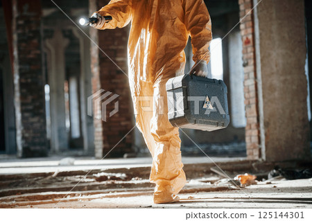 With flashlight. Man dressed in chemical protection suit in the ruins of the post apocalyptic building 125144301