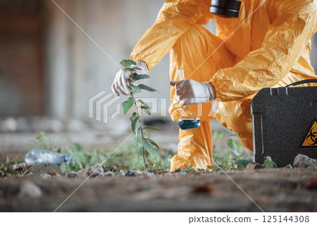 Examines the plant. Man dressed in chemical protection suit in the ruins of the post apocalyptic building Examines the plant. Man dressed in chemical protection suit in the ruins of the post apocalyptic building 125144308