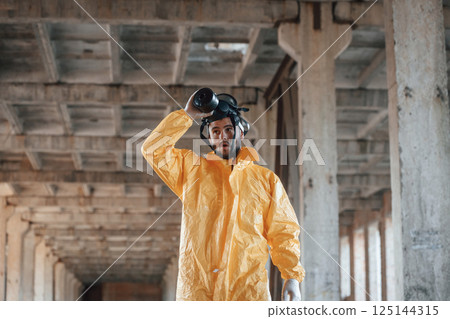 Taking off gas mask. Man dressed in chemical protection suit in the ruins of the post apocalyptic building 125144315