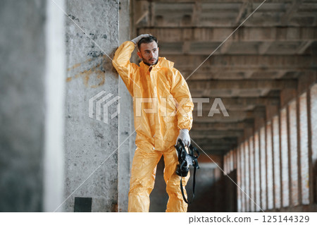 Tired, frightened. Leaning on the wall. Man dressed in chemical protection suit in the ruins of the post apocalyptic building Tired, frightened. Leaning on the wall. Man dressed in chemical protection suit in the ruins of the post apocalyptic building 125144329