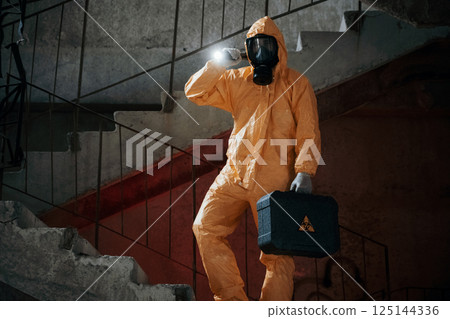 On stairs with flashlight and case. Man dressed in chemical protection suit in the ruins of the post apocalyptic building 125144336