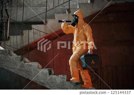 On stairs with flashlight and case. Man dressed in chemical protection suit in the ruins of the post apocalyptic building 125144337