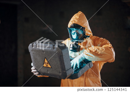 Case with blue glowing light. Hazard materials. Man dressed in chemical protection suit in the ruins of the post apocalyptic building 125144341