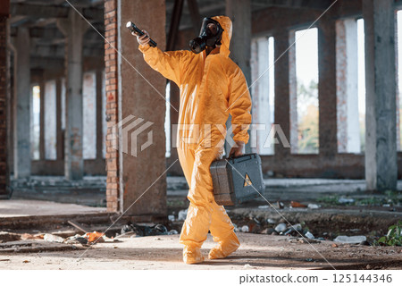 View from the side. Man dressed in chemical protection suit in the ruins of the post apocalyptic building 125144346