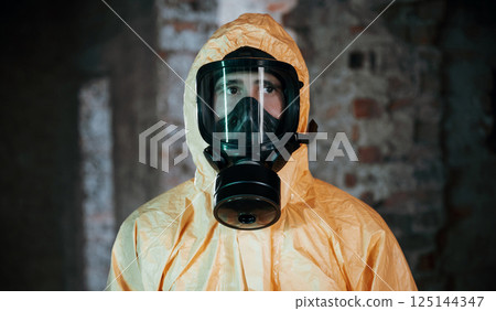 In respirator, portrait. Man dressed in chemical protection suit in the ruins of the post apocalyptic building 125144347