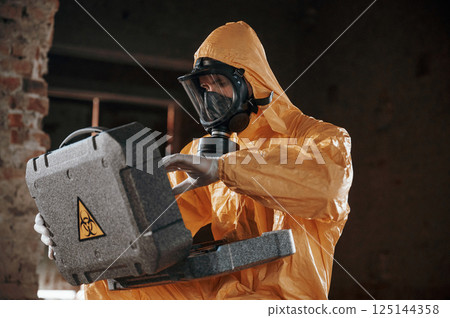 Sitting with radioactive case. Man dressed in chemical protection suit in the ruins of the post apocalyptic building 125144358