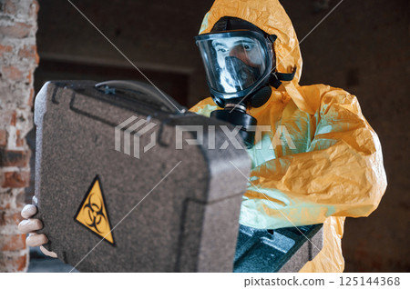 Frightened scientist is with radioactive materials. Man dressed in chemical protection suit in the ruins of the post apocalyptic building 125144368