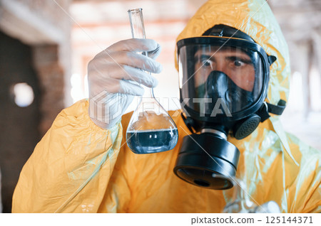 Frightened scientist is with radioactive materials. Man dressed in chemical protection suit in the ruins of the post apocalyptic building 125144371