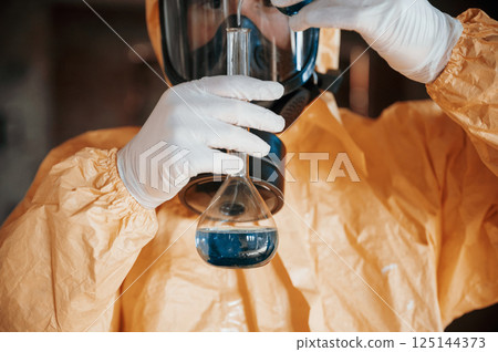 Holding a test tube and examining radioactive liquid. Man dressed in chemical protection suit in the ruins of the post apocalyptic building 125144373