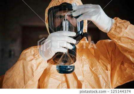 Holding a test tube and examining radioactive liquid. Man dressed in chemical protection suit in the ruins of the post apocalyptic building 125144374