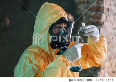 Examining radioactive liquid. Man dressed in chemical protection suit in the ruins of the post apocalyptic building 125144375