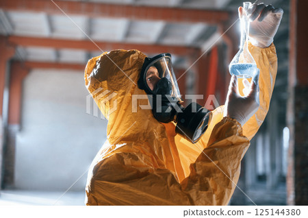 Examining radioactive liquid. Man dressed in chemical protection suit in the ruins of the post apocalyptic building 125144380