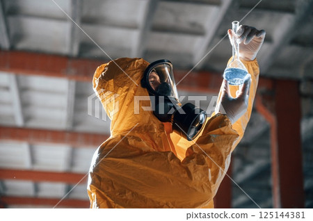 Examining radioactive liquid. Man dressed in chemical protection suit in the ruins of the post apocalyptic building 125144381